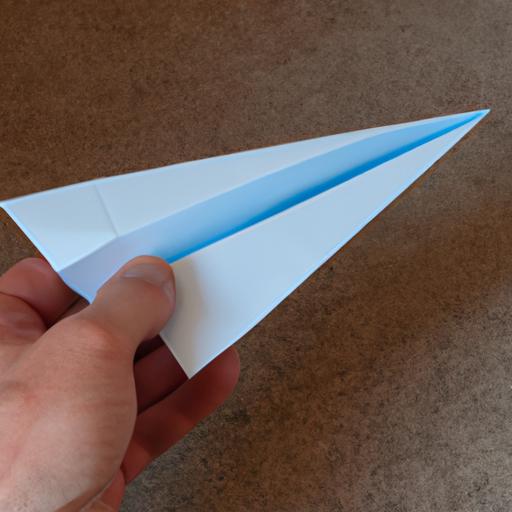 A hand demonstrating the first step in making a paper airplane